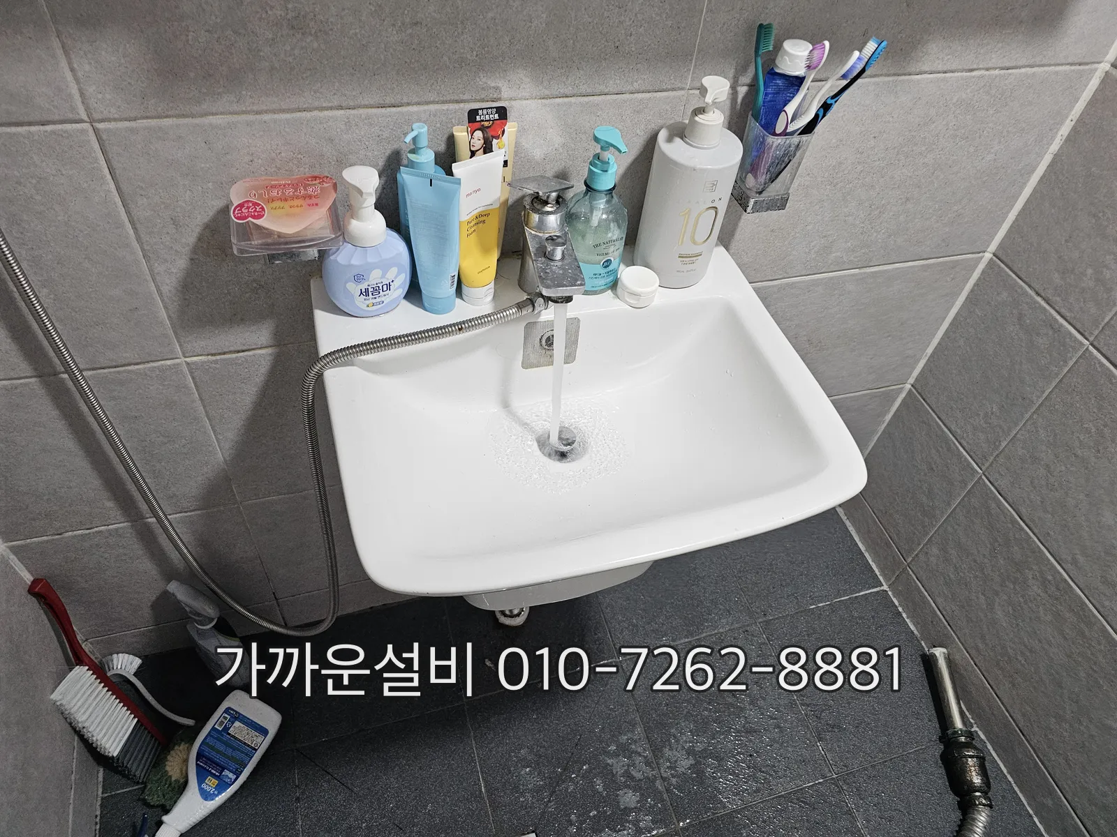 벽걸이 세면대에 물을 틀어 배수 상태를 확인하는 모습, 아래로 배수관이 벽으로 들어가는 구조