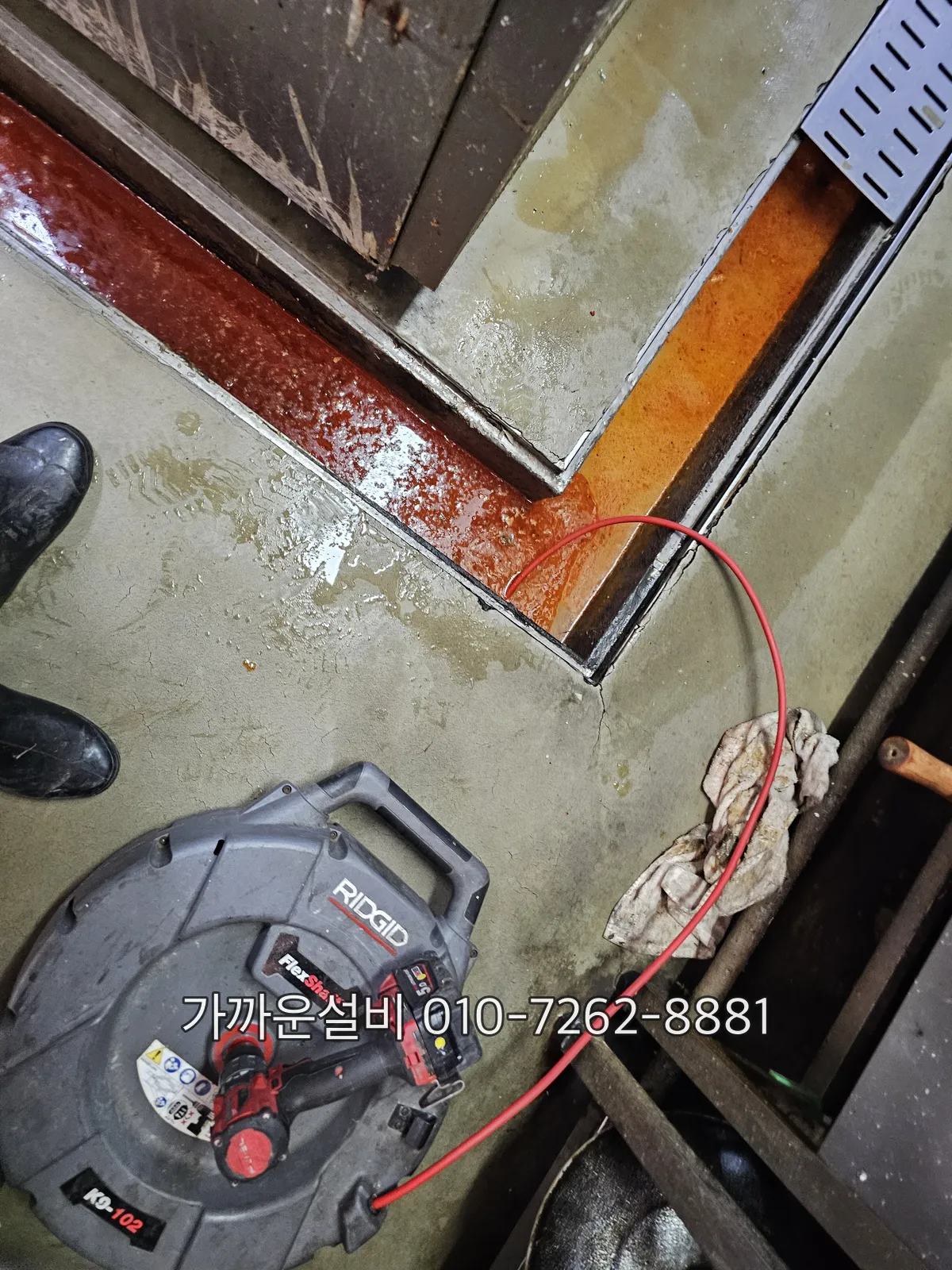 주방 바닥 트렌치에서 그리스트랩 뒤쪽 배관으로 고압세척 호스를 넣는 모습